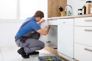 Repairman In Overalls Repairing Cabinet Hinge In Kitchen